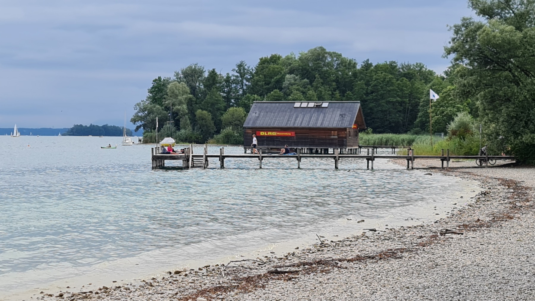 Bootshaus mit Steg am Kiesufer eines Sees