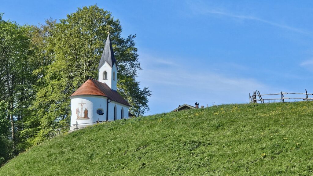 Weiße Kapelle auf grünem Hügel unter blauem Himmel